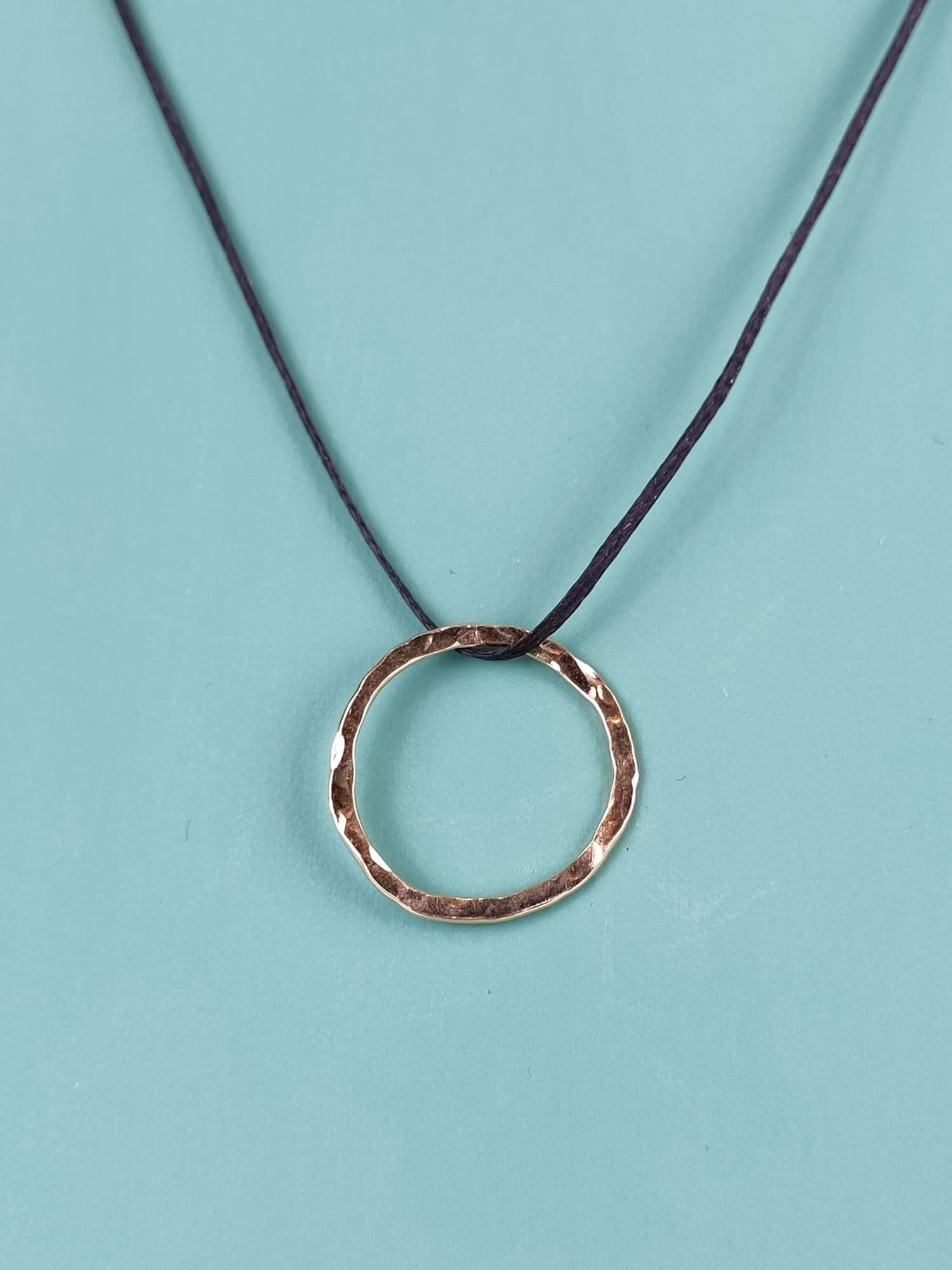 Original phone photo of a hammered gold pendant on a black cord